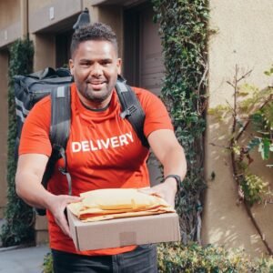Friendly deliveryman in red delivering packages outdoors on a sunny day.